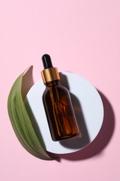 Photo of Bottle of cosmetic oil and leaf on pink background, flat lay