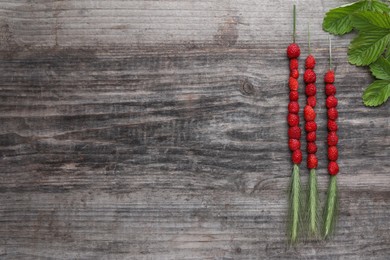 Photo of Grass stems with wild strawberries and leaves on wooden table, flat lay. Space for text