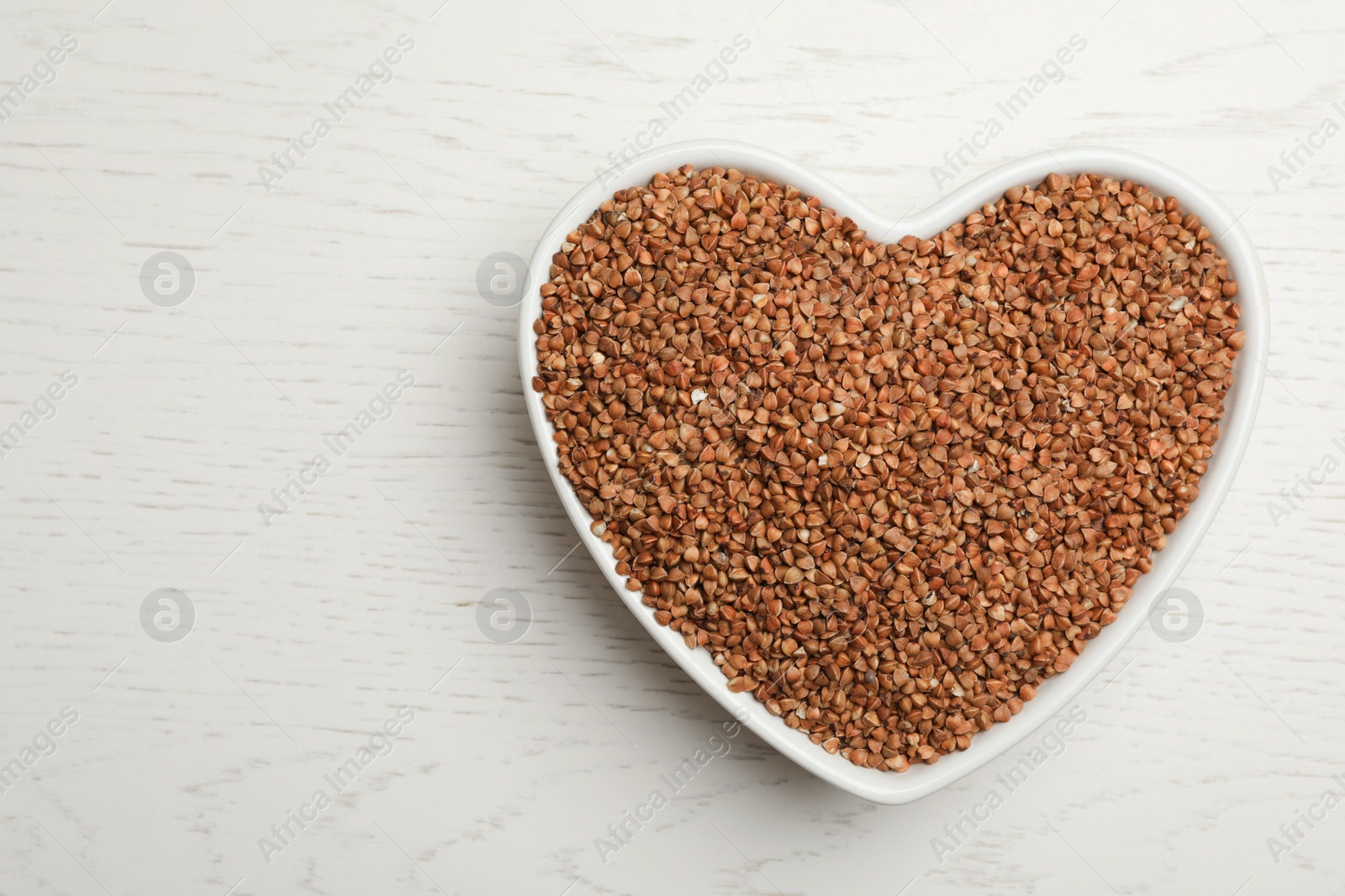 Photo of Buckwheat grains on white wooden table, top view. Space for text