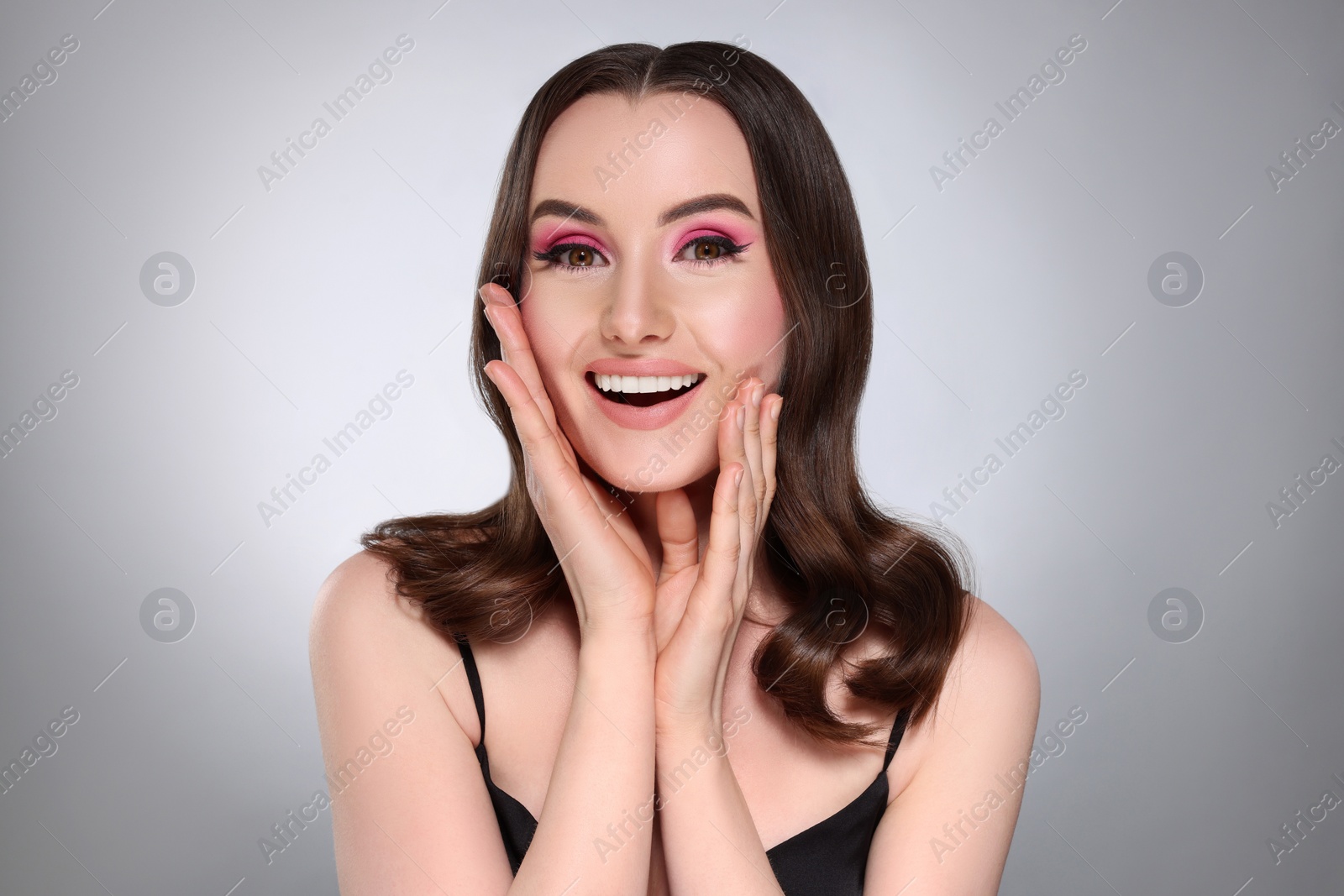 Photo of Portrait of beautiful young woman with makeup and gorgeous hair styling on light grey background