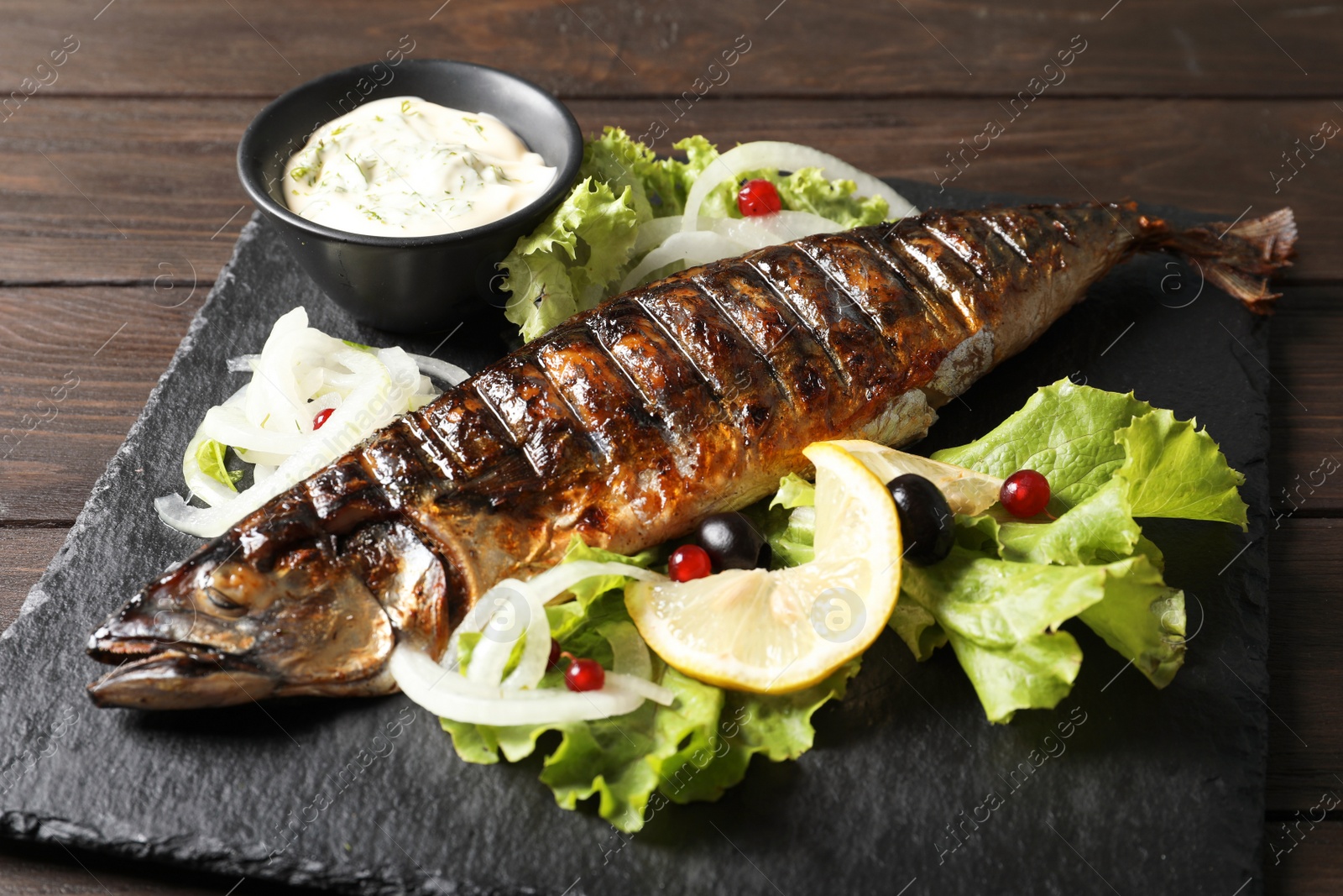 Photo of Slate plate with delicious grilled fish and sauce on table, closeup