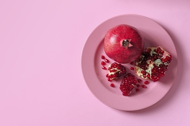 Photo of Plate with ripe pomegranates on color background, top view. Space for text