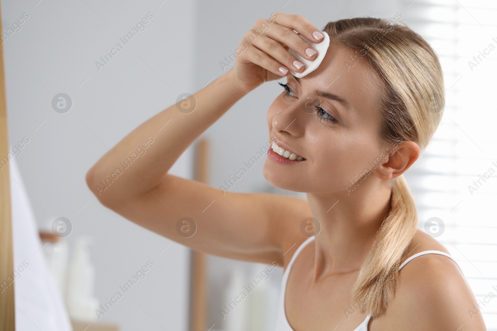 Photo of Smiling woman removing makeup with cotton pad indoors