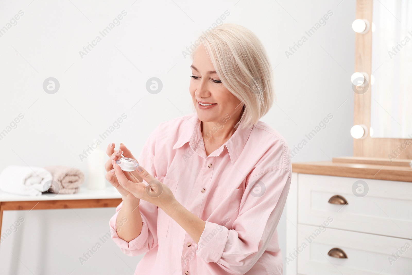 Photo of Portrait of charming mature woman with healthy beautiful face skin and natural makeup applying cream indoors