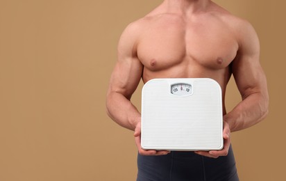 Photo of Athletic man holding scales on brown background, closeup and space for text. Weight loss concept