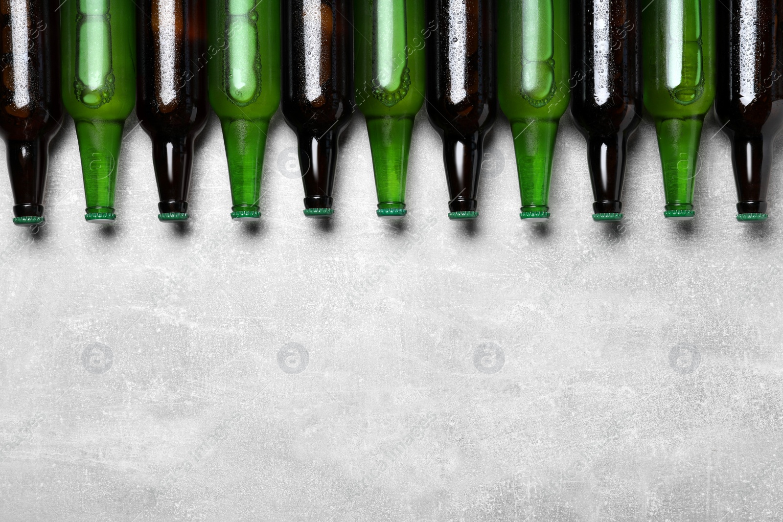 Photo of Glass bottles of beer on light grey background, flat lay. Space for text