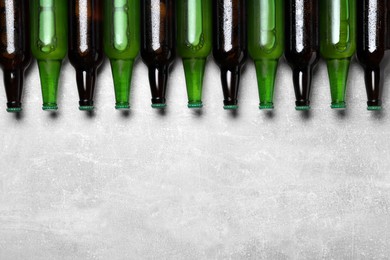 Glass bottles of beer on light grey background, flat lay. Space for text