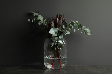 Bouquet of protea flowers and eucalyptus branches in glass vase on table against black background