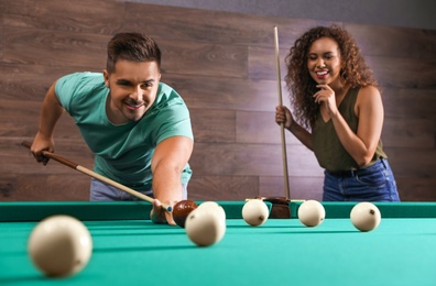 Young man and woman playing billiard indoors