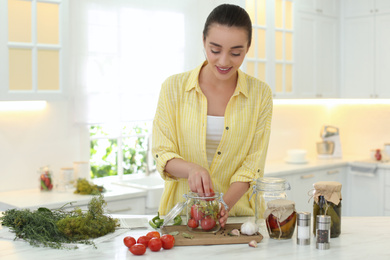 Photo of Woman putting vegetables into pickling jar at table in kitchen