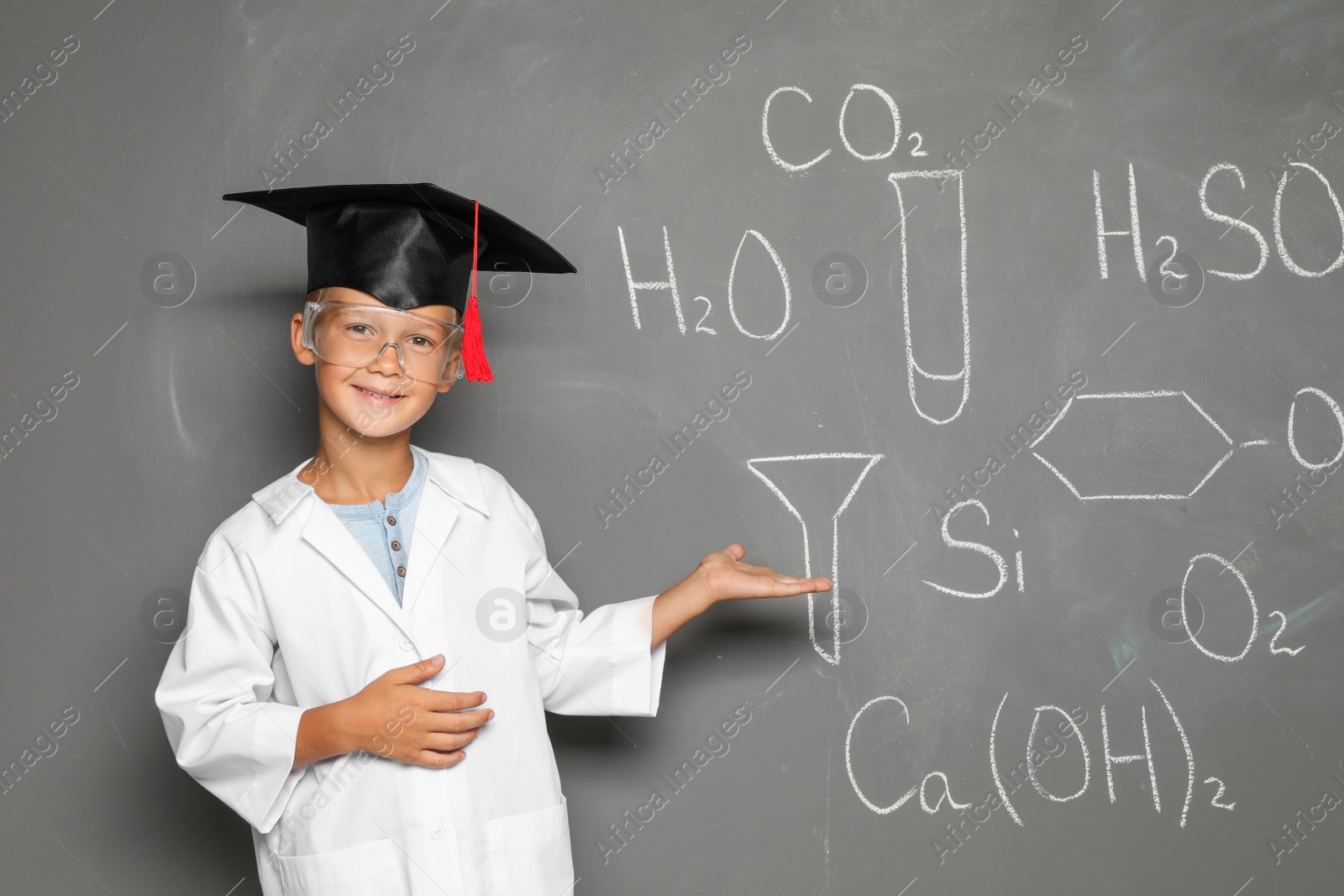 Photo of Little school child in laboratory uniform with graduate cap and chemical formulas on grey background