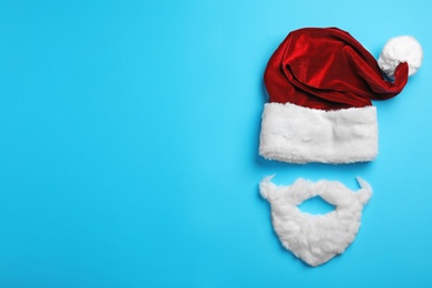 Photo of Santa Claus hat and beard on light blue background, flat lay. Space for text