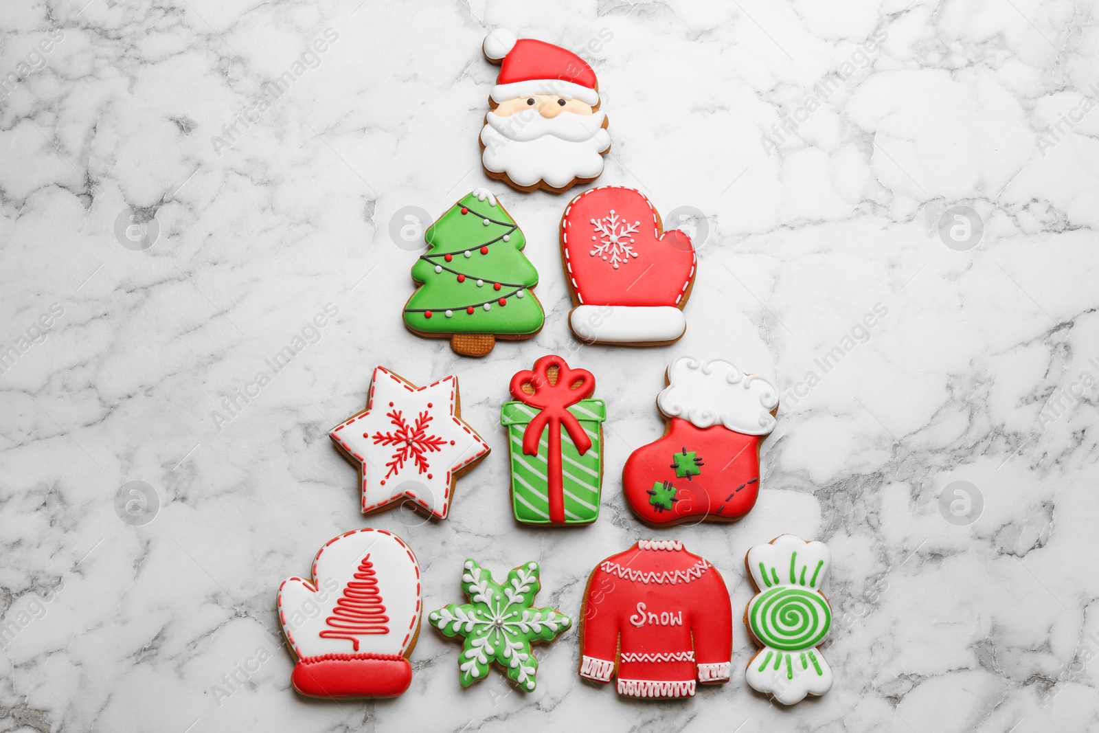 Photo of Christmas tree shape made of delicious decorated gingerbread cookies on white marble table, flat lay