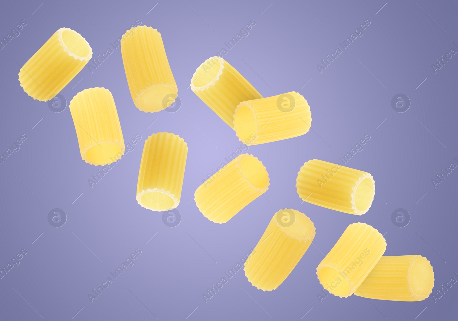 Image of Raw rigatoni pasta falling on purple background