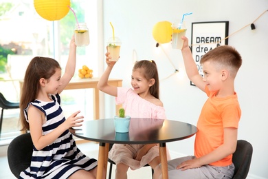 Photo of Little kids with natural lemonade at table indoors