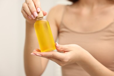 Aromatherapy. Woman with bottle of essential oil on light background, closeup