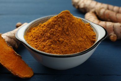 Bowl with turmeric powder and raw roots on blue wooden table, closeup