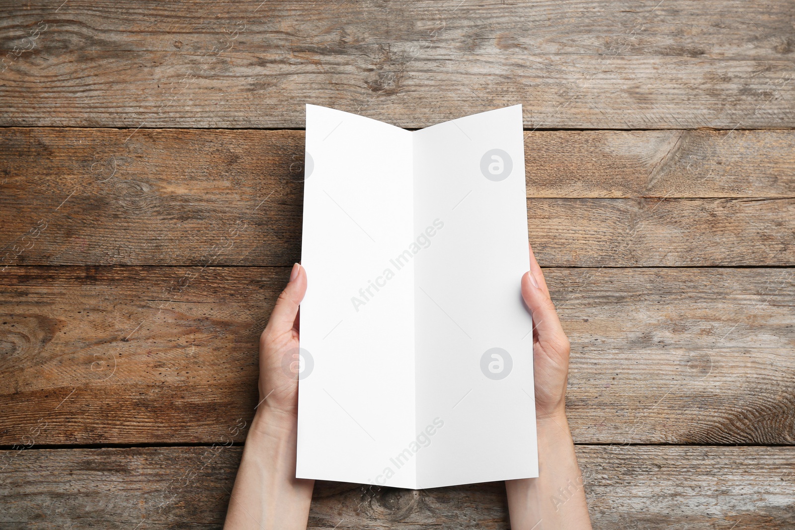 Photo of Young woman holding blank brochure at wooden table, top view. Mock up for design