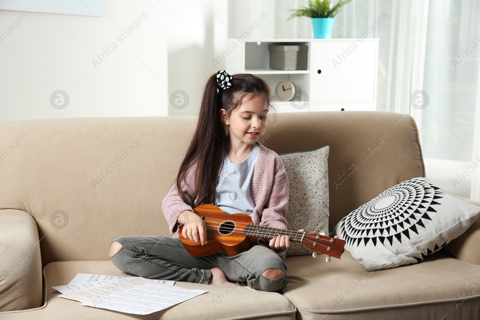 Photo of Cute little girl playing guitar on sofa in room
