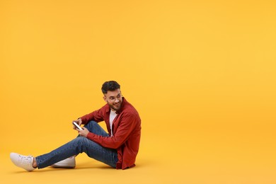 Photo of Happy young man using smartphone on yellow background, space for text