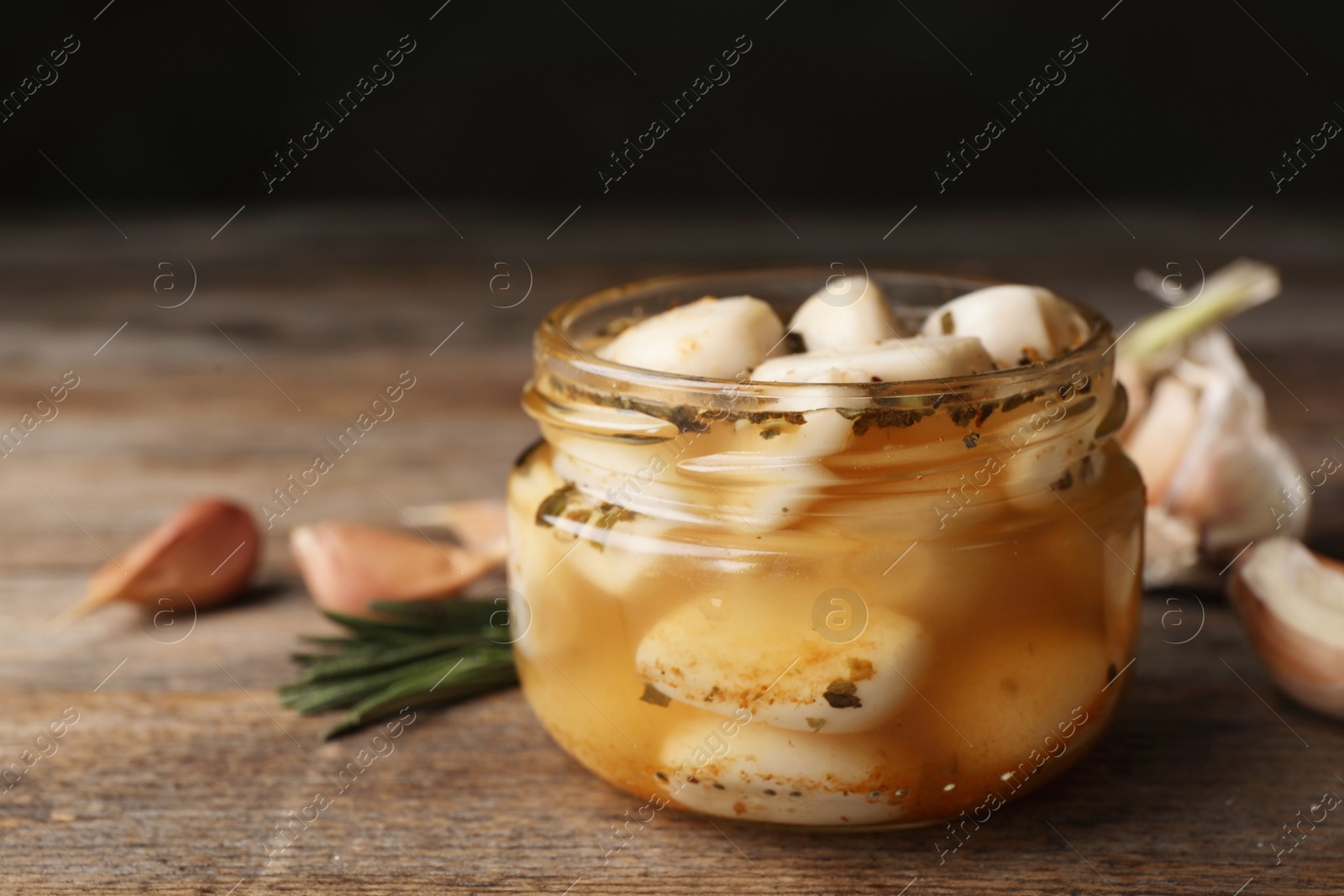 Photo of Preserved garlic in glass jar on wooden table, closeup. Space for text