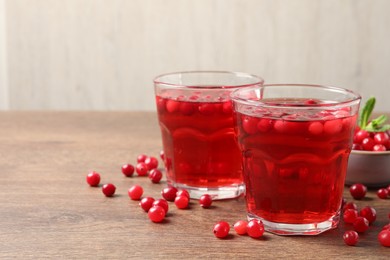 Tasty cranberry juice in glasses and fresh berries on wooden table, closeup. Space for text