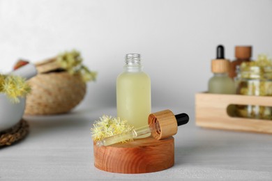 Photo of Bottle of essential oil and linden flowers on white wooden table