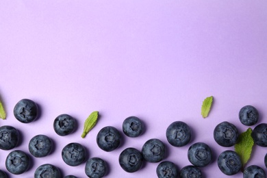 Tasty ripe blueberries and leaves on violet background, flat lay with space for text