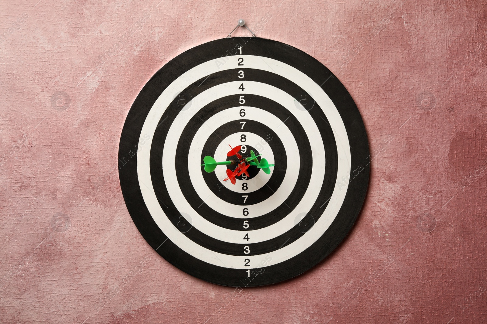 Photo of Dart board with arrows hitting target on pink wall