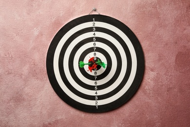 Photo of Dart board with arrows hitting target on pink wall