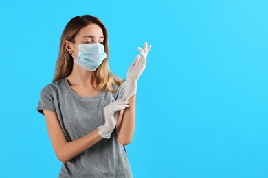 Photo of Young woman in protective mask putting on medical gloves against light blue background. Space for text