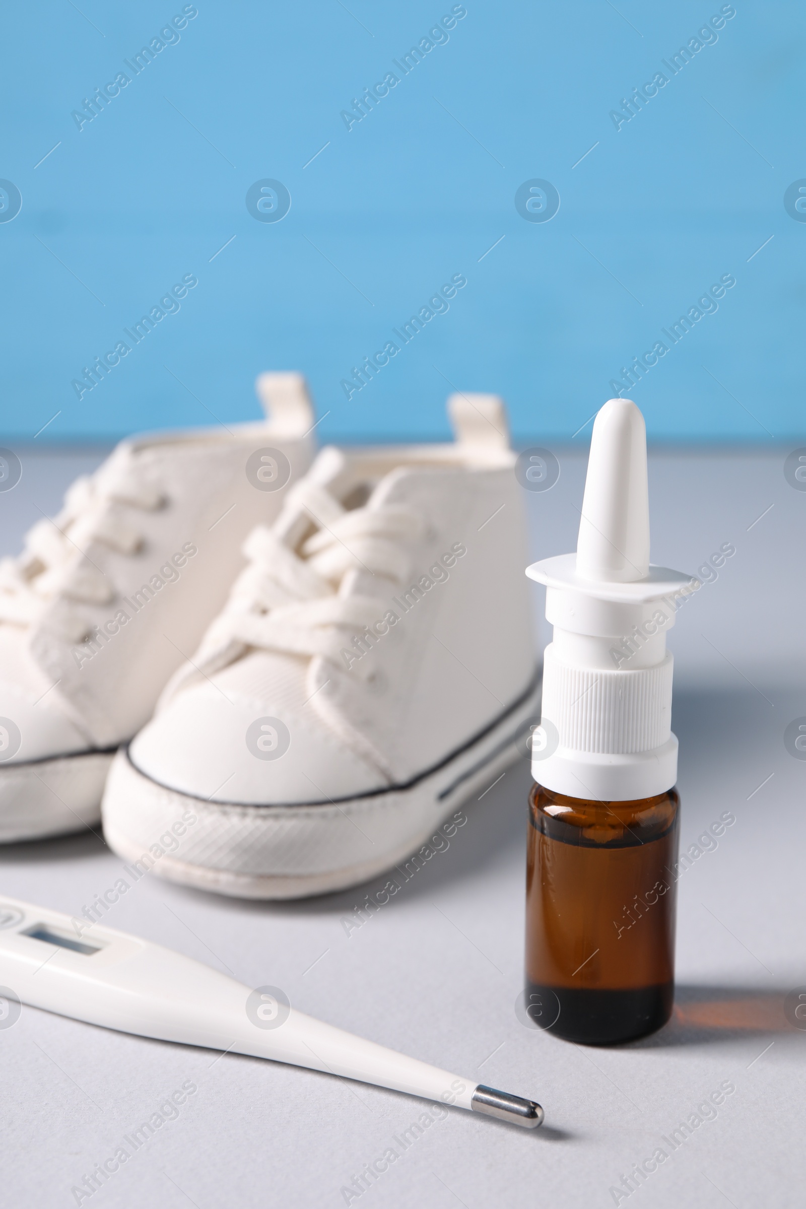 Photo of Thermometer, nasal spray and child`s sneakers on grey table, closeup