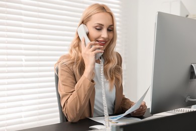 Secretary with document talking on smartphone at table in office