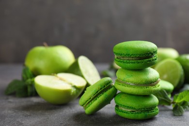 Photo of Delicious green macarons, fresh fruits and mint on grey table. Space for text