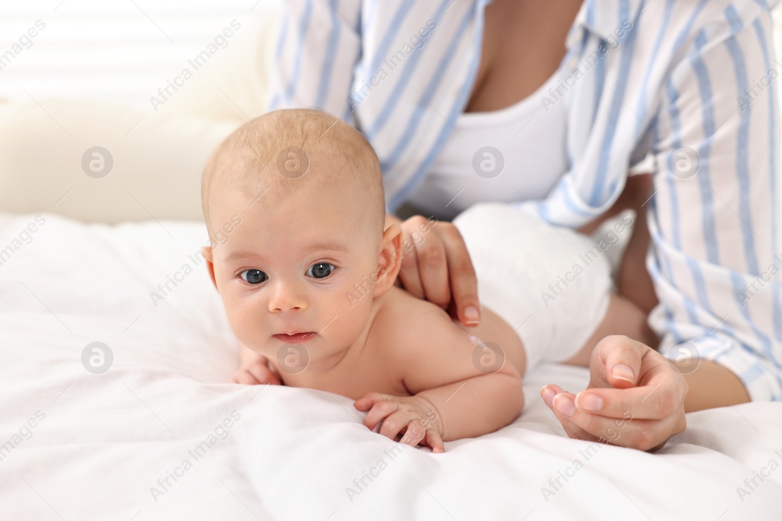 Photo of Woman applying body cream onto baby`s skin on bed, closeup