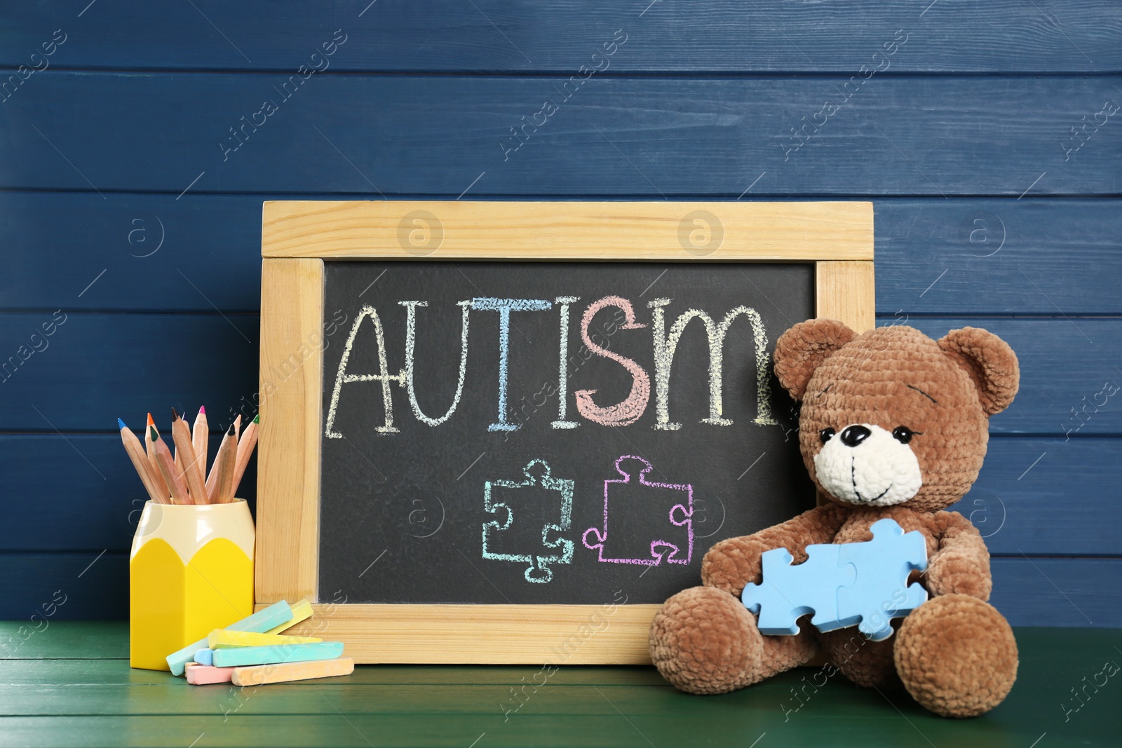 Photo of Small blackboard with word Autism, toy bear and stationery on green wooden table