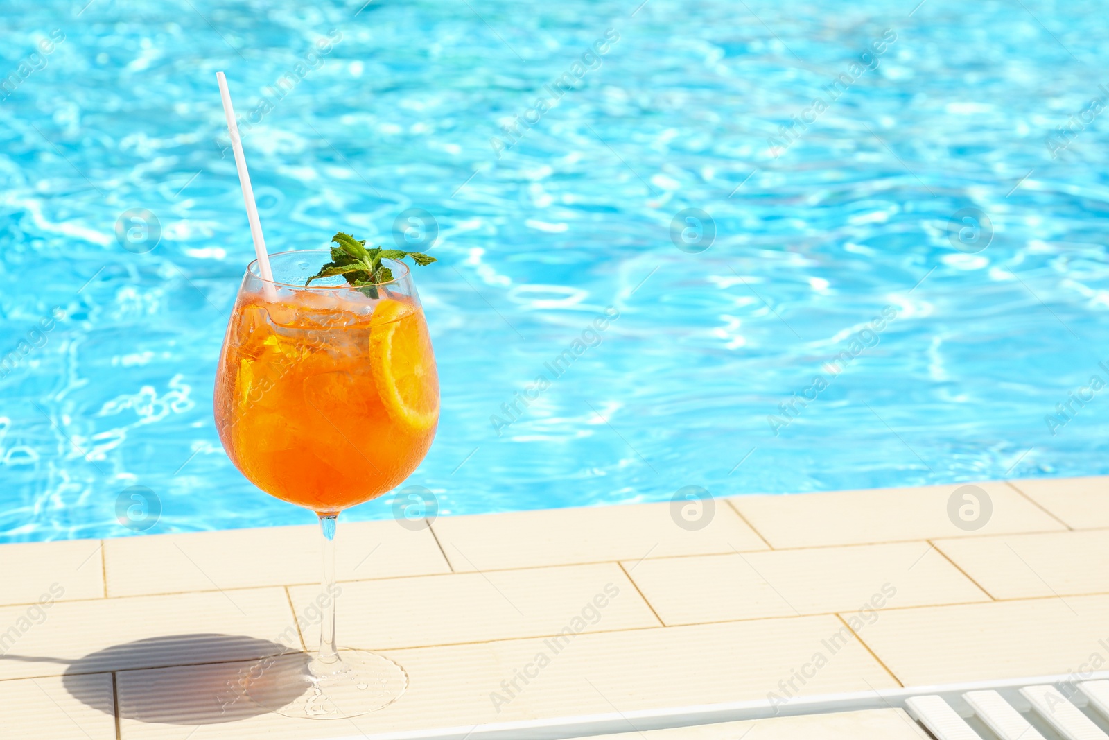 Photo of Glass of delicious cocktail near swimming pool, space for text. Refreshing drink