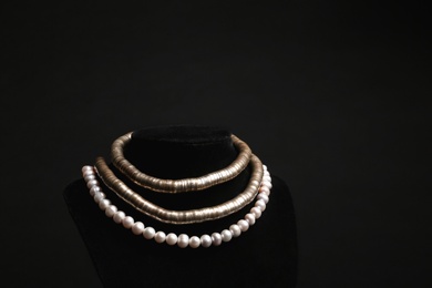 Stylish necklaces on stand against black background, space for text. Luxury jewelry