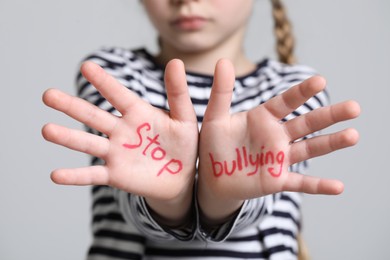 Photo of Girl showing hands with phrase Stop Bullying on light grey background, closeup