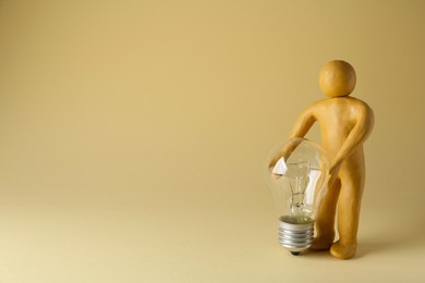 Photo of Human figure made of plasticine holding light bulb on beige background. Space for text