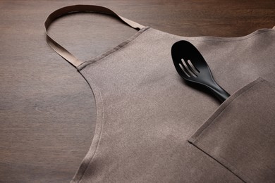 Stylish brown apron and slotted spoon on wooden table. Space for text