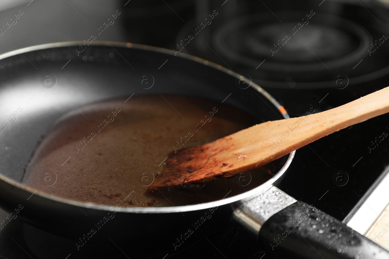 Photo of Frying pan with spatula and used cooking oil on stove, closeup