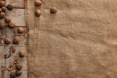 Photo of Burlap fabric and walnuts on wooden table, top view. Space for text