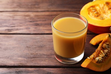 Photo of Tasty pumpkin juice in glass and cut pumpkin on wooden table. Space for text