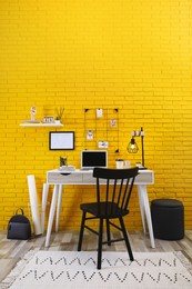 Photo of Stylish home office interior with comfortable workplace near yellow brick wall