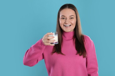 Photo of Happy woman with milk mustache holding glass of drink on light blue background