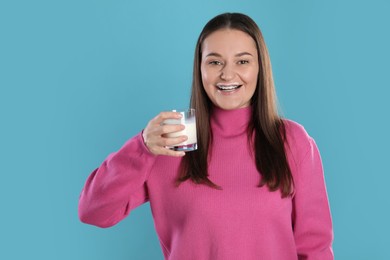 Happy woman with milk mustache holding glass of drink on light blue background