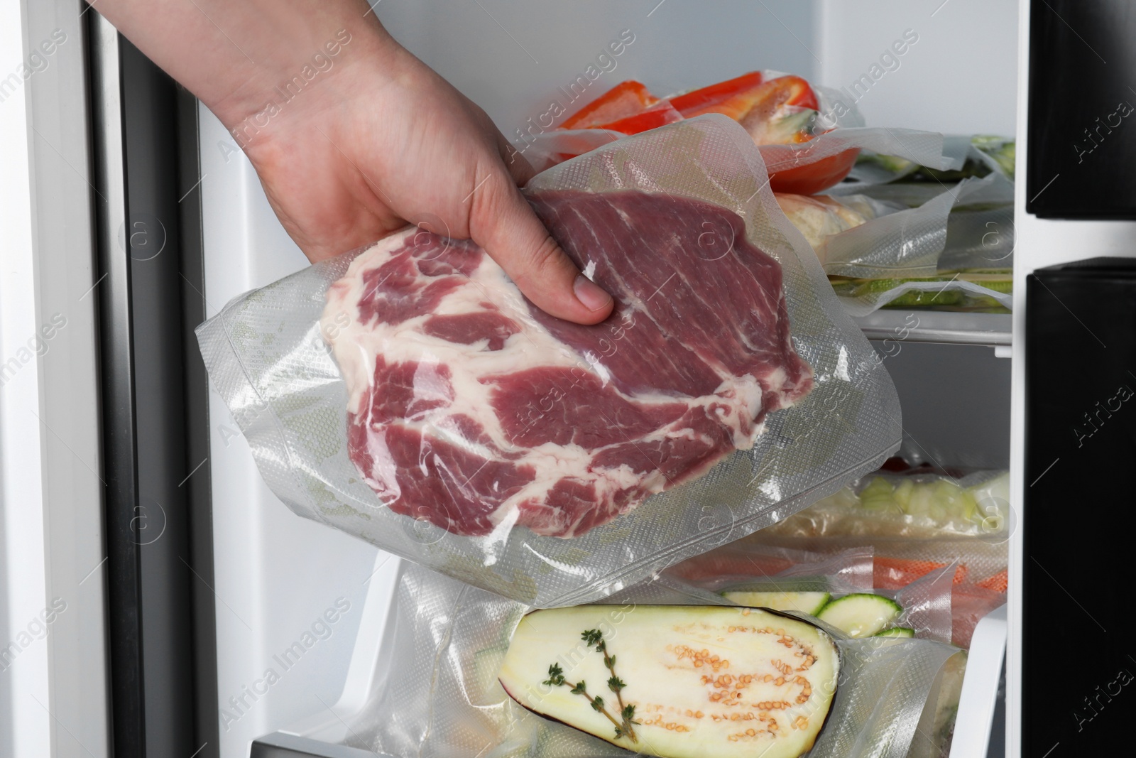 Photo of Woman putting vacuum bag with meat into fridge, closeup. Food storage