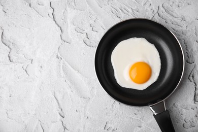 Photo of Tasty fried egg in pan on white textured table, top view. Space for text