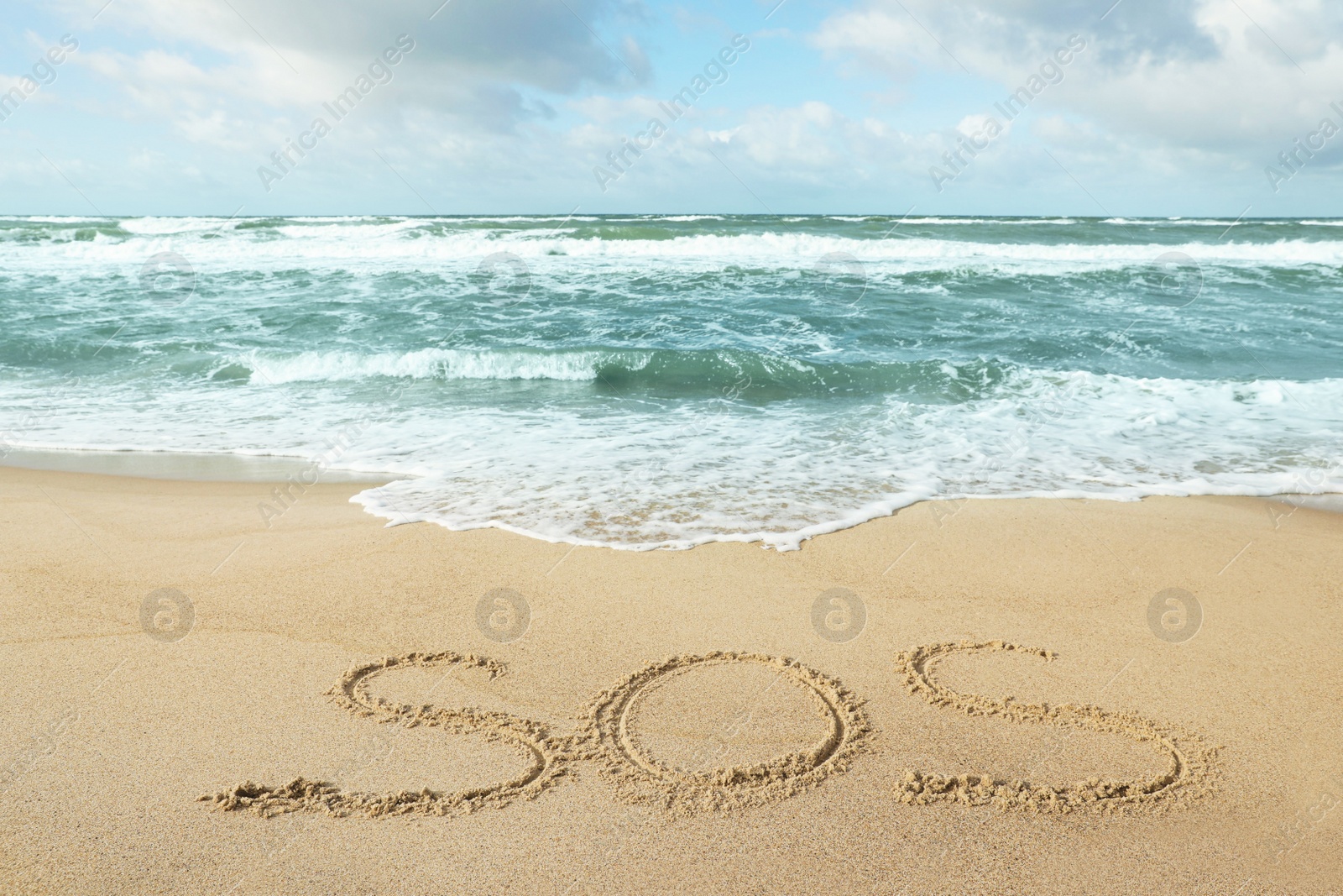 Photo of Message SOS drawn on sand near wavy sea